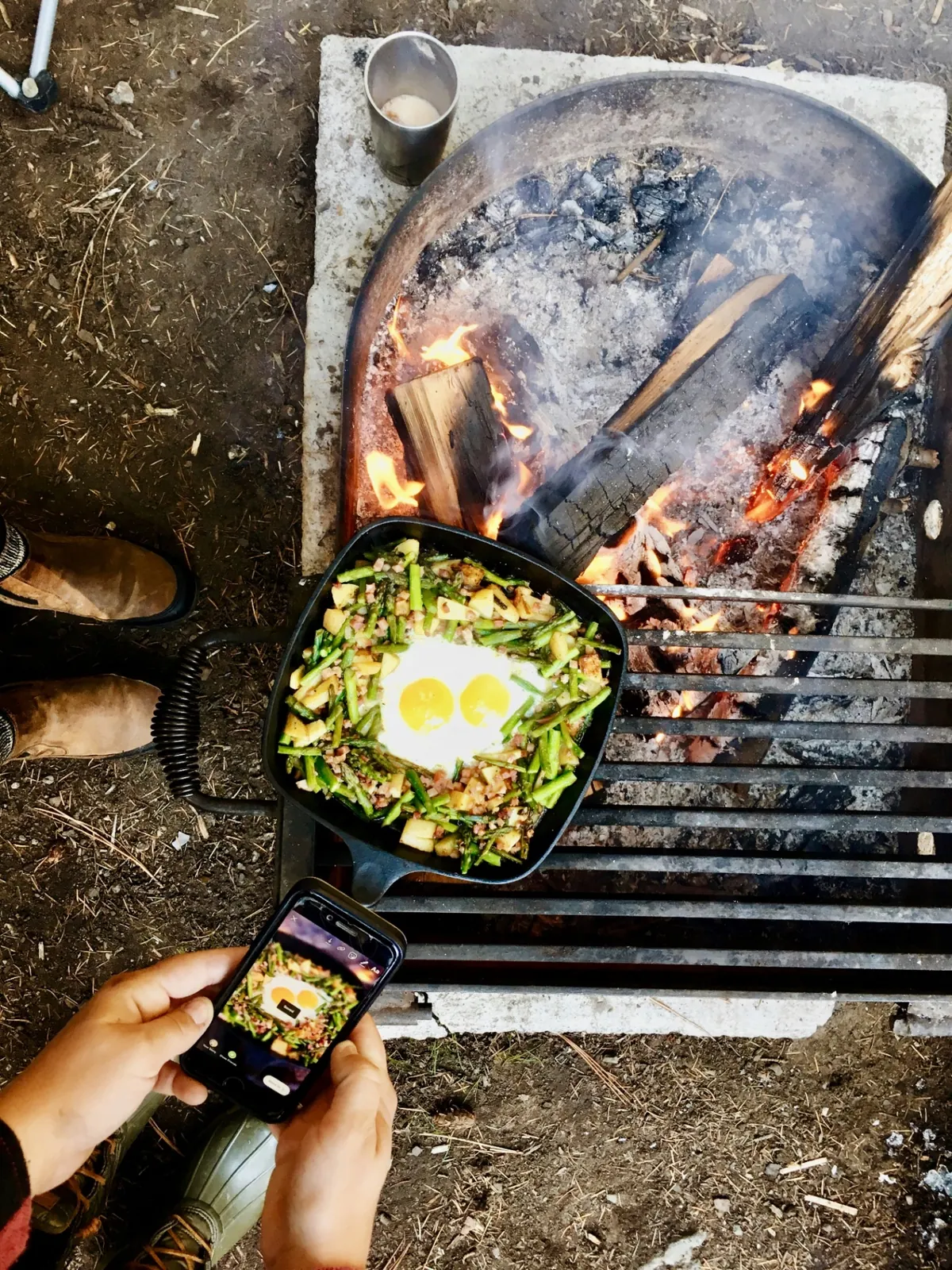 Cast-iron skillet of asparagus, potatoes and eggs cooking next to a campfire
